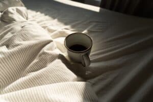 Tasse Kaffee auf Nachttisch neben Wecker – wie Koffein den Schlaf beeinflusst und zerstört