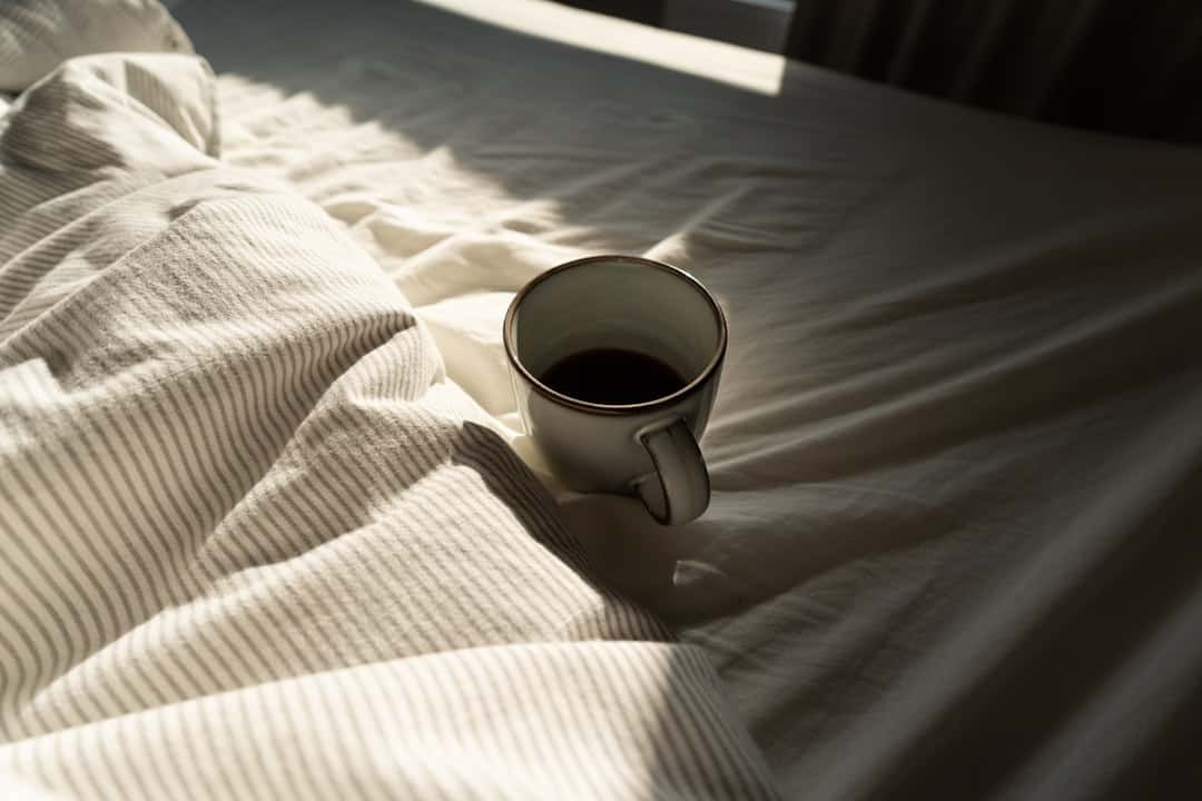 Tasse Kaffee auf Nachttisch neben Wecker – wie Koffein den Schlaf beeinflusst und zerstört