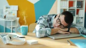 Person macht einen 20-minütigen Powernap am Schreibtisch im hellen Büro